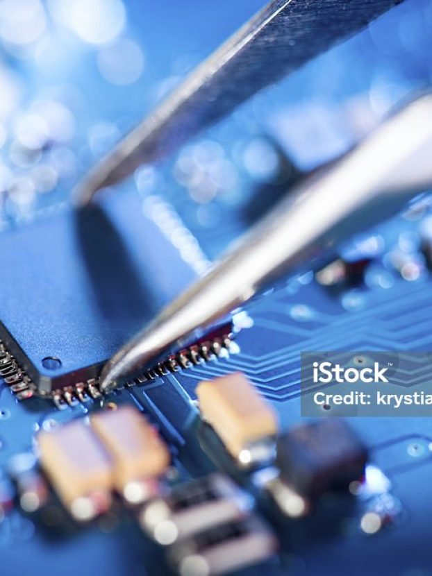 Electronic technician holding tweezers and assemblin a circuit board.